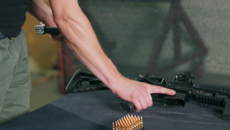 close-up of male hands loading bullets into a gun magazine clip at a firing range. a man loads a magazine clip onto a rifle and fires a round at an indoor firing range