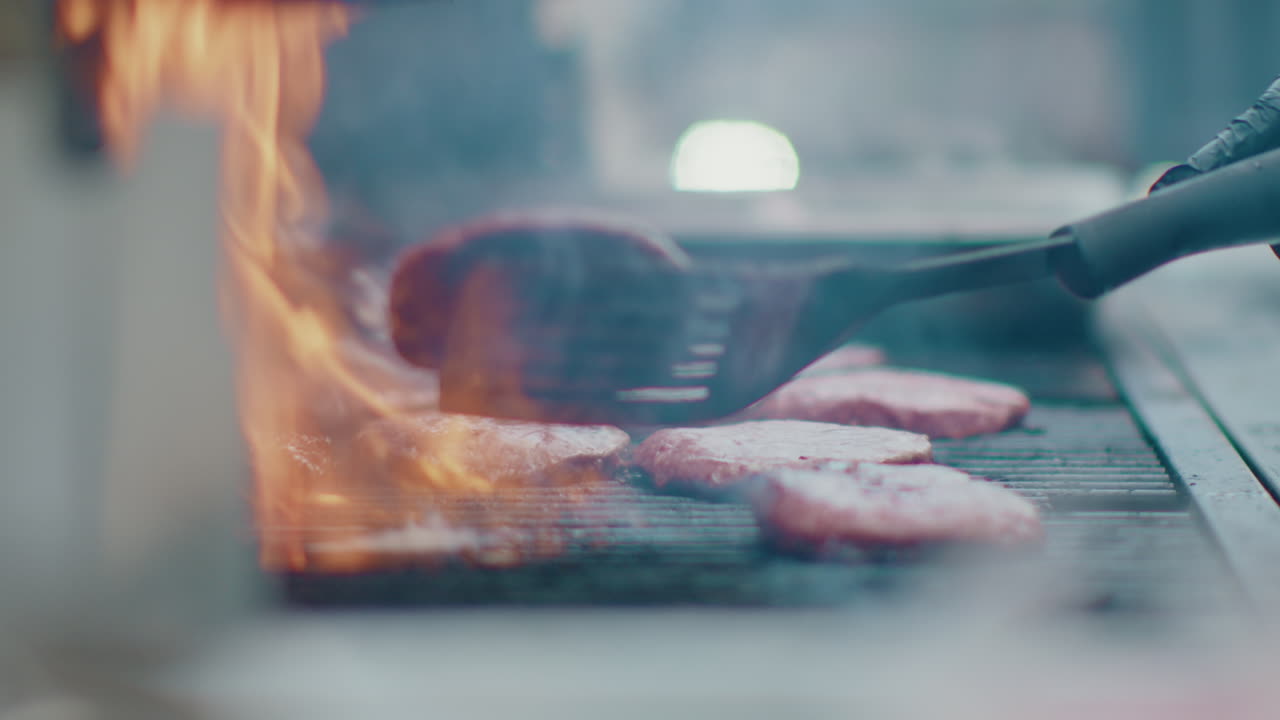 A scene of a metal spatula flipping delicious, smoking hamburgers on an outdoor BBQ grill. Smoke and fire create an enticing atmosphere, highlighting the mouthwatering grilling process.