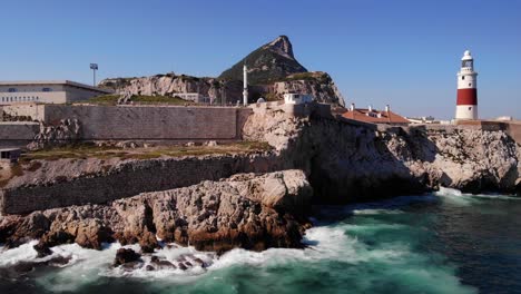 Waves-from-the-swell-of-the-Mediterranean-splash-on-the-cliffs-below-the-lighthouse-against-the-background-of-the-great-Muslim-mosque-and-the-upper-rock-of-Gibraltar-Close-up-drone-lifted-panning-shot