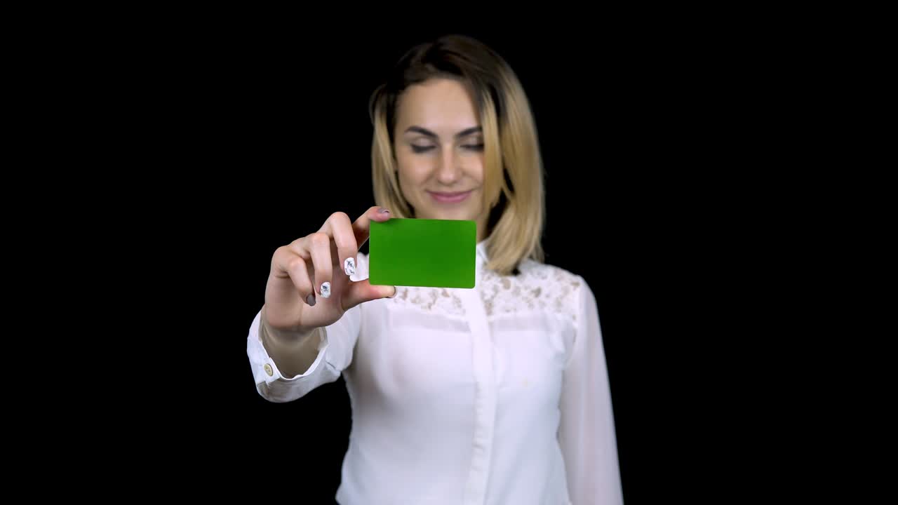 una joven empresaria con una camisa blanca sostiene una tarjeta bancaria en la mano. fondo negro aislado. tarjeta verde chromakey.