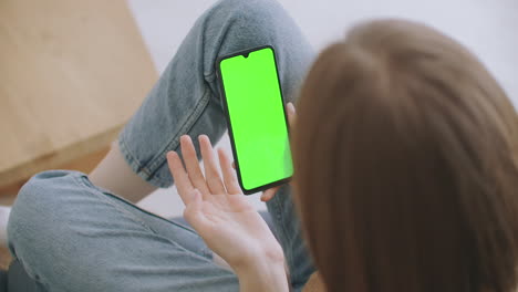 Close-up-shot-of-green-screen-template-smartphone-in-female-hands-at-home-girl-is-watching-content-without-touching-gadget-screen.-Modern-technology-and-information-concept.