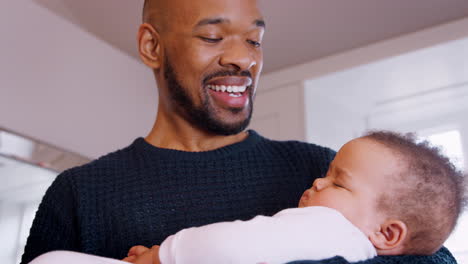 New-Father-Cuddling-Sleeping-Baby-Girl-In-Nursery-At-Home