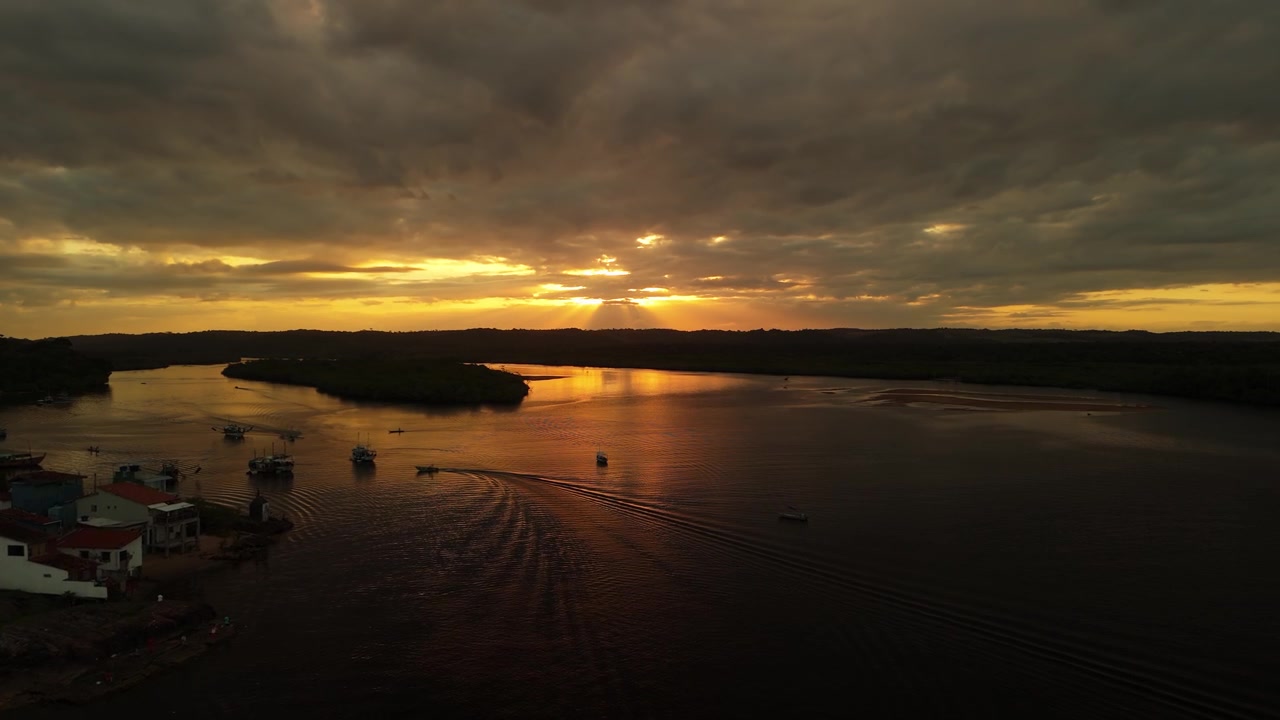 Drone descends over Rio de Contas at sunset, with a small boat crossing the water in Itacaré, Bahia