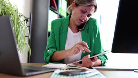 woman multitasking in an office, talking on the phone and writing in a notebook