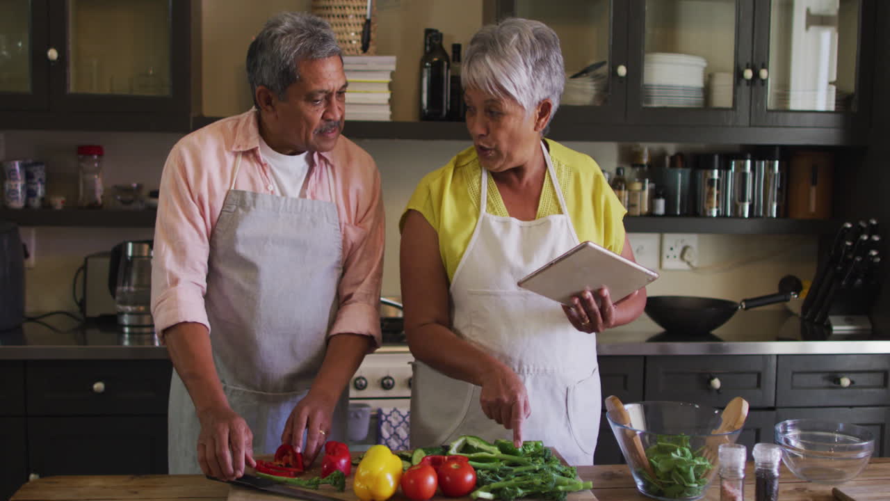 una pareja de dos razas que usa una tableta preparando comida en la cocina.