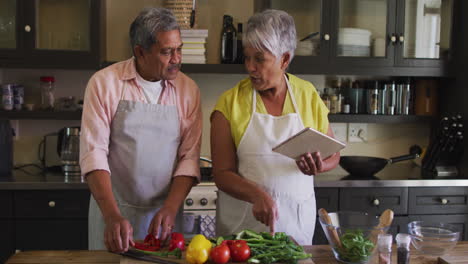 senior biracial couple using tablet preparing food in kitchen