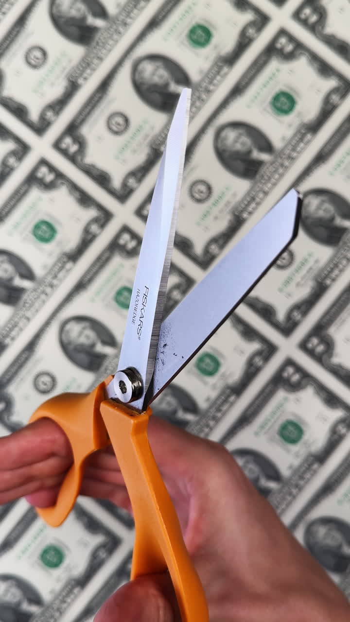 San Antonio, USA, 14 August 2025: Scissors with orange finger holes are opened and closed. Uncut sheet of two dollar banknotes at backdrop. Vertical video