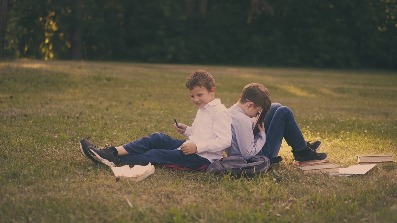 소년들은 공원에서 시험을 준비하면서 교과서를 즐기고 있습니다.