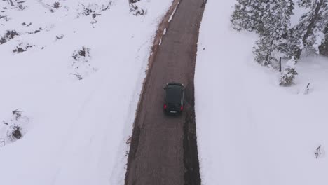 Aufsteigende-Drohnenaufnahme-Eines-Schwarzen-Autos-Auf-Einer-Bergstraße-Während-Eines-Ruhigen-Wintertages-In-Italien