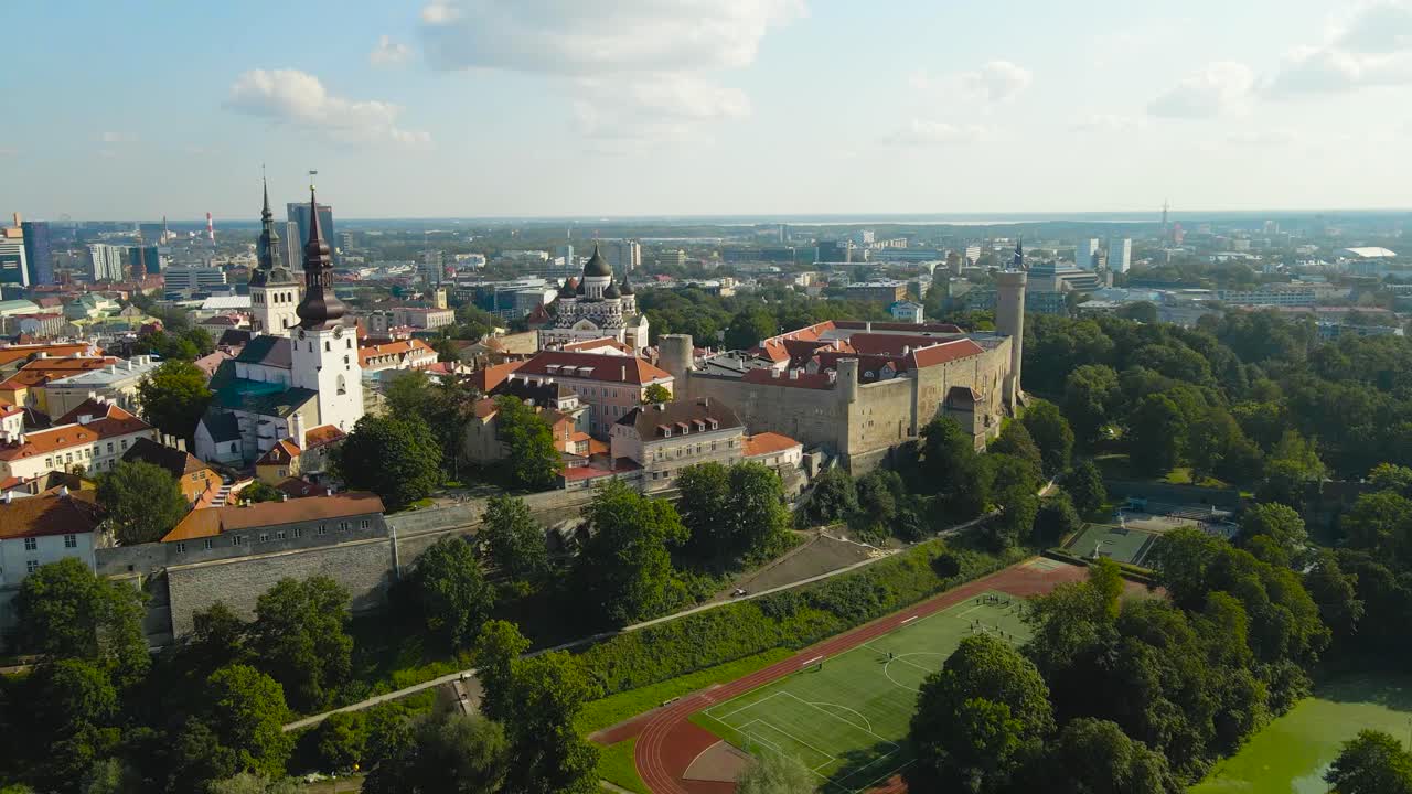 Aerial drone video of historic Tallinn old town and city walls where church towers are in the middle of red rooftops, urban greenery and Estonian parialment building visible as well, sunny summer day
