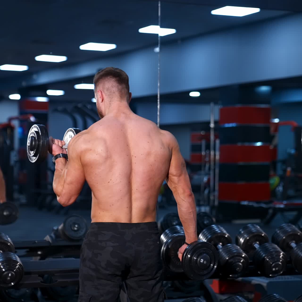 Giovane uomo forte con corpo atletico che fa esercizi con i manubri. Fitness, bodybuilding. Cura della salute. Slow motion.