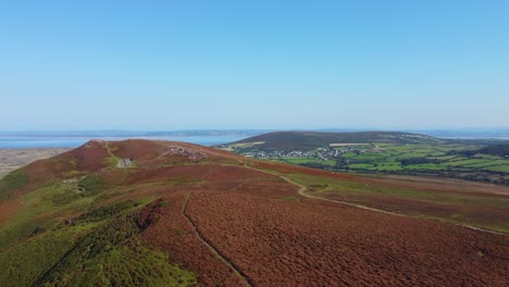 rising aerial drone view across gower peninsula including llangenith rural welsh village with fields and winding trails and paths for hikers on beautiful sunny day with blue sky 4k
