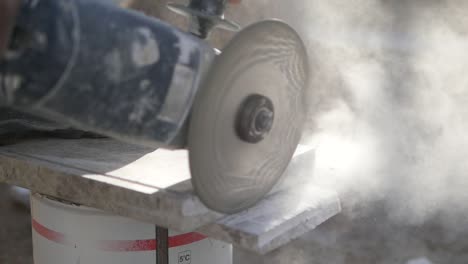 a close-up of a man cutting a stone tile with a power grinder.