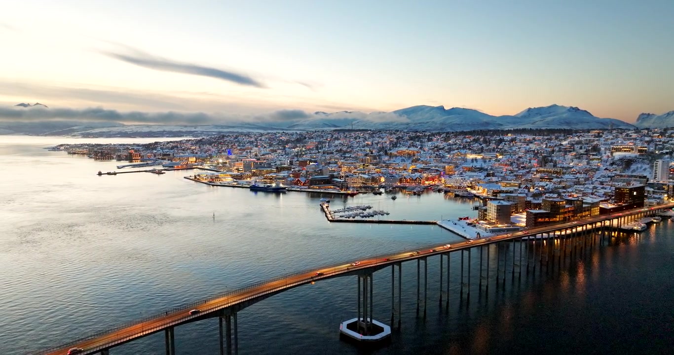 Tromsø-Brücke mit beleuchteter und verschneiter Stadt bei Sonnenaufgang während der Weihnachtszeit, Norwegen. Platz für Text. Rückwärtsflug aus der Luft.
