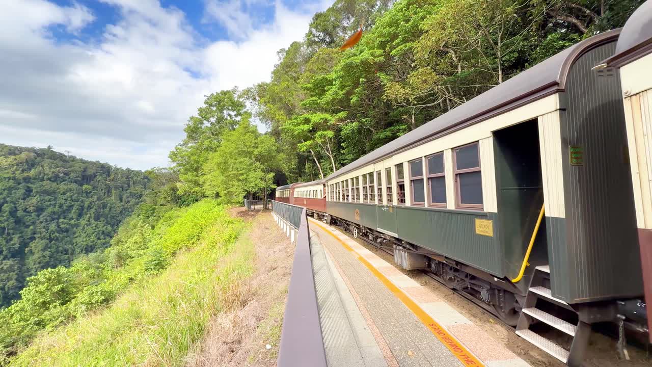 Classic train approaches platform through lush rainforest, daylight, wide angle, steady camera, vibrant colors