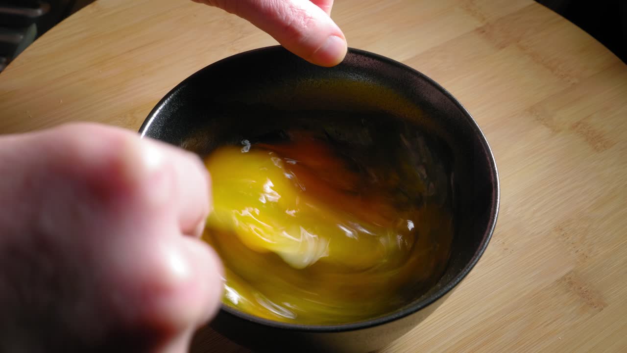 la mano masculina está batiendo huevos con un tenedor, cocinando huevos para el desayuno
