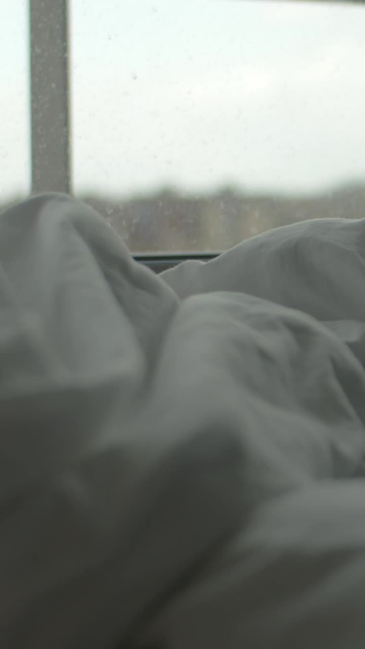 Fokus Lembut pada Seprai Tempat Tidur Kusut yang Menampilkan Pemandangan Kota dari Jendela