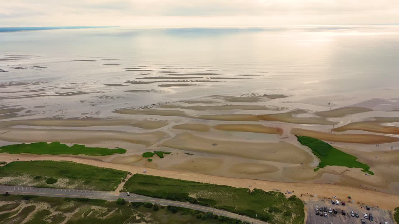 Drone video of a generic beach at receding tide shows intricate ripple marks, tide pools shimmering in shallow hollows, and sculpted sand dunes reaching toward the horizon