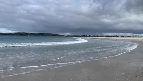 Niedrige-Welle,-Die-Unter-Einem-Bewölkten-Grauen-Himmel-In-Omaha-Warkworth,-Neuseeland,-Auf-Den-Strand-Fließt