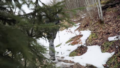 backpacker in hiking gear with trekking poles walking up outdoor trail with snow