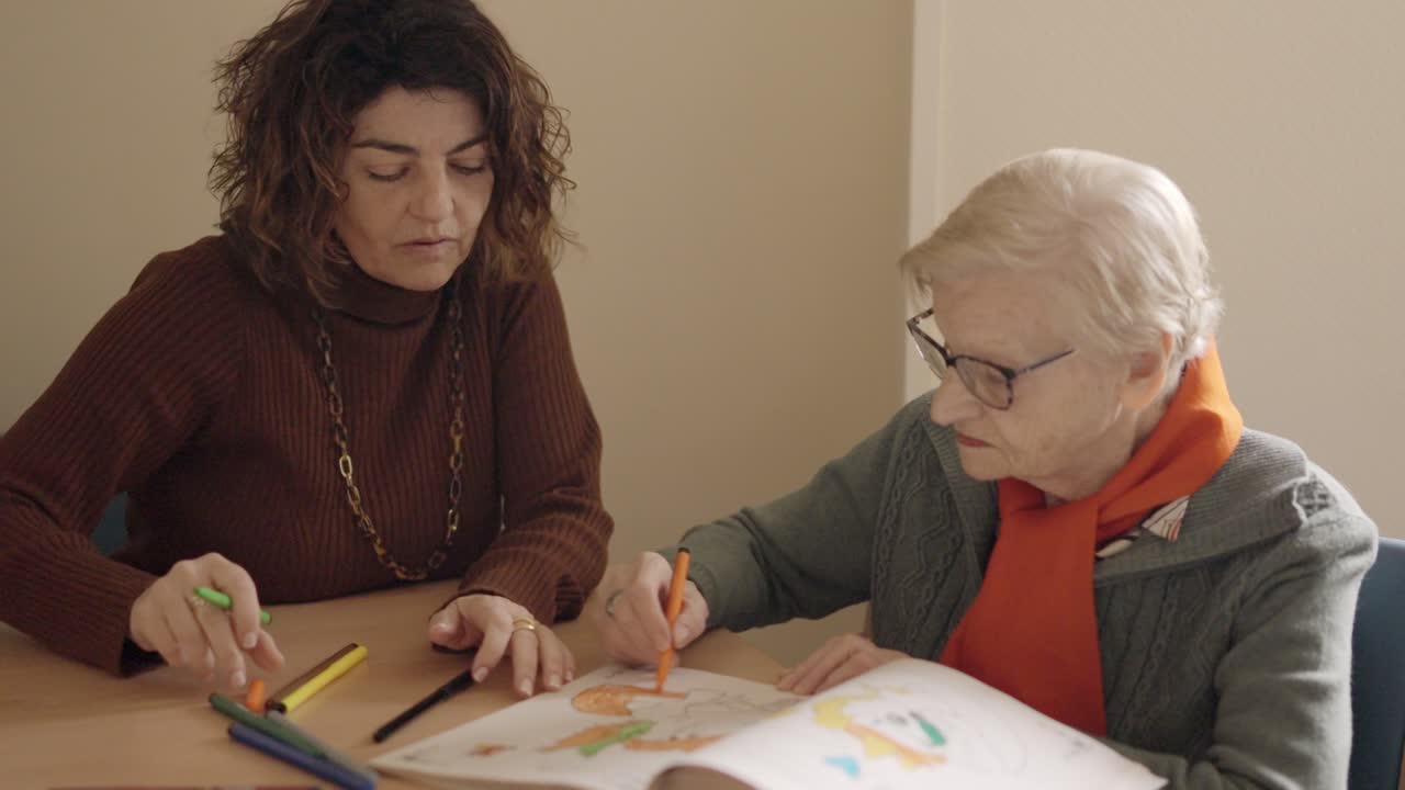 Caregiver and senior woman coloring a draw in a geriatric