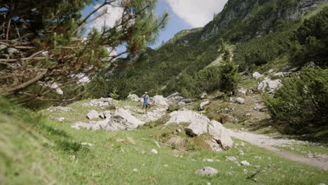 Excursionista-Caminando-Por-El-Camino-Rocoso-En-Las-Montañas,-árboles-De-Coníferas-Creciendo-En-La-Ladera,-Verano-Soleado-Con-Algunas-Nubes-En-El-Cielo-Azul