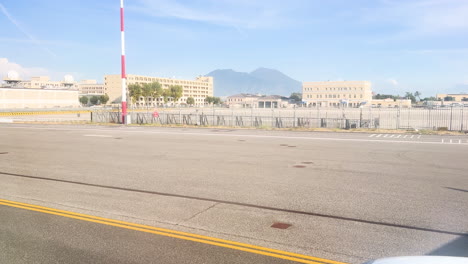 Airport-runway-with-a-red-and-white-striped-pole,-fenced-area,-and-a-Mount-Vesuvius-backdrop-under-a-clear-sky