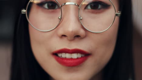 primer plano de la hermosa joven con anteojos mirando hacia abajo y luego levantando los ojos a la cámara y sonriendo alegremente, borrosa y enfocada
