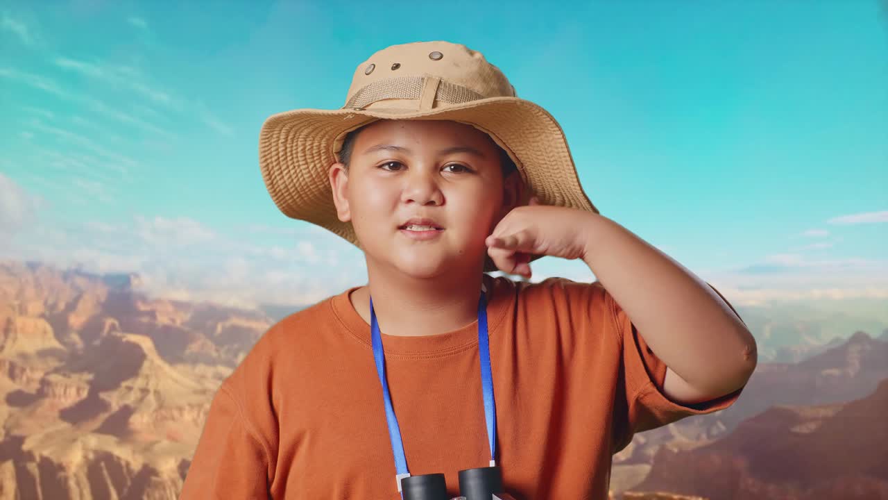 Asian Boy With A Hat And Binoculars Using The Magnifying Glass Then Making Call Me Gesture While Traveling At The Top Of Mountain. Boy Researcher Examines Something, Travel Adventure, Close Up