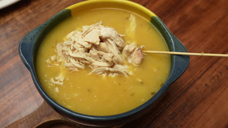 a steaming bowl of colombian ajiaco soup, rich with tender chicken and potatoes in golden broth. captured in warm light, highlighting texture and vibrant colors for an inviting look