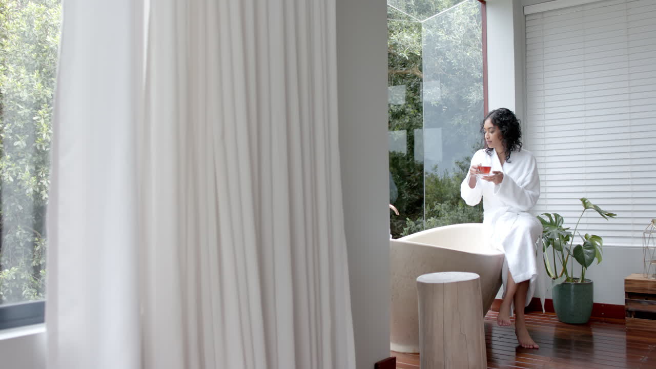 목욕복을 입은 두 인종의 여성이 욕조에 앉아 집에서 차를 마시고, 느린 동작, 복사 공간