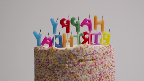 melted blown out candles spelling happy birthday on revolving birthday cake covered with decorations against grey studio background