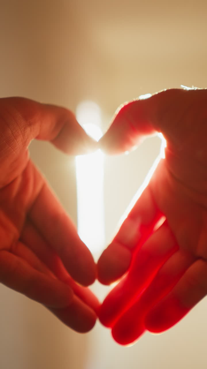 en primera persona pov de manos que forman una forma de corazón con deslumbrantes rayos de luz solar atravesando, filmado con una cámara de mano