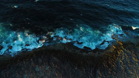 Drone-push-in-tilt-down-over-water-ebb-and-flow-crashing-on-volcanic-rocky-rough-shoreline-of-curacao