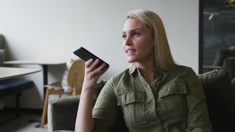 Caucasian-businesswoman-sitting-on-couch-talking-on-smartphone-in-modern-office