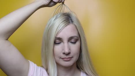 a caucasian blond woman enjoy head scalp massage by anti stress acupuncture metal octopus tool, equipment, she closes her eyes with pleasure, yellow background