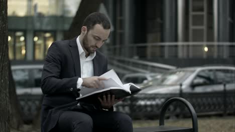 man is sitting on a bench in park and approvingly reading business plan, business papers