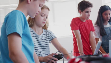 group of students in after school computer coding class learning to program robot vehicle