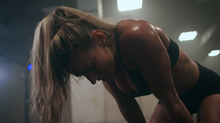 Tired exhausted woman after a hard workout in the gym is sitting on the floor and breathing hard. Professional athlete is preparing for competitions. Hard work and the overcoming of itself and pain.