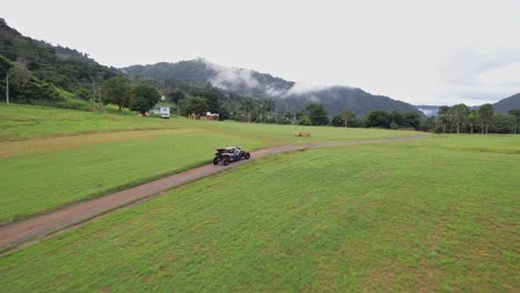 embark on an adrenaline-fueled journey as the drone seamlessly tracks an off-road vehicle along a dusty trail, framed by towering mountains and a mystical veil of fog