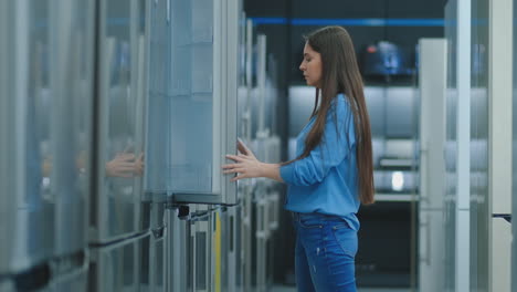 a young woman to open the refrigerator door to store appliances and compare with other models to buy the new house