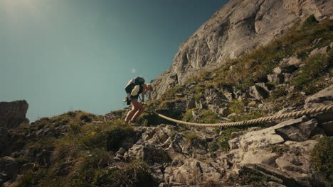 woman hiking up a steep mountain trail with rope