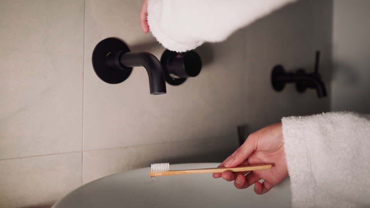 Lady washes toothbrush with water flow in bathroom closeup. Woman in terry bathrobe finishes dental care routine by cleaning toothbrush at home
