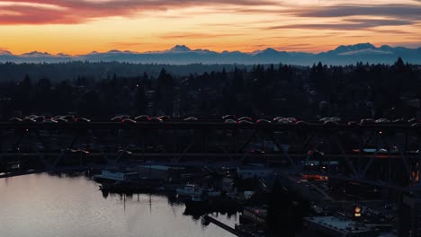 Traffic-moves-across-the-I5-bridge-over-Lake-Union-in-Seattle,-Washington-with-a-beautiful-sunset-mountain-range-backdrop