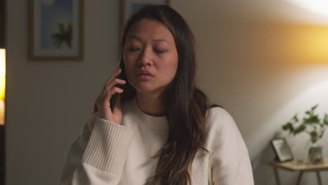 close up of anxious or stressed woman spending evening at home sitting on sofa in lounge talking on mobile phone