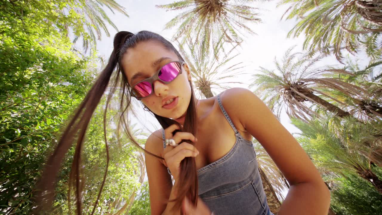 Giovane donna con occhiali da sole che posa tra le palme