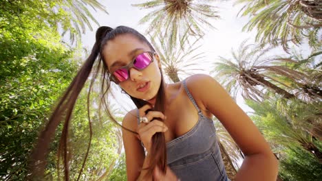 young woman in sunglasses posing among palm trees