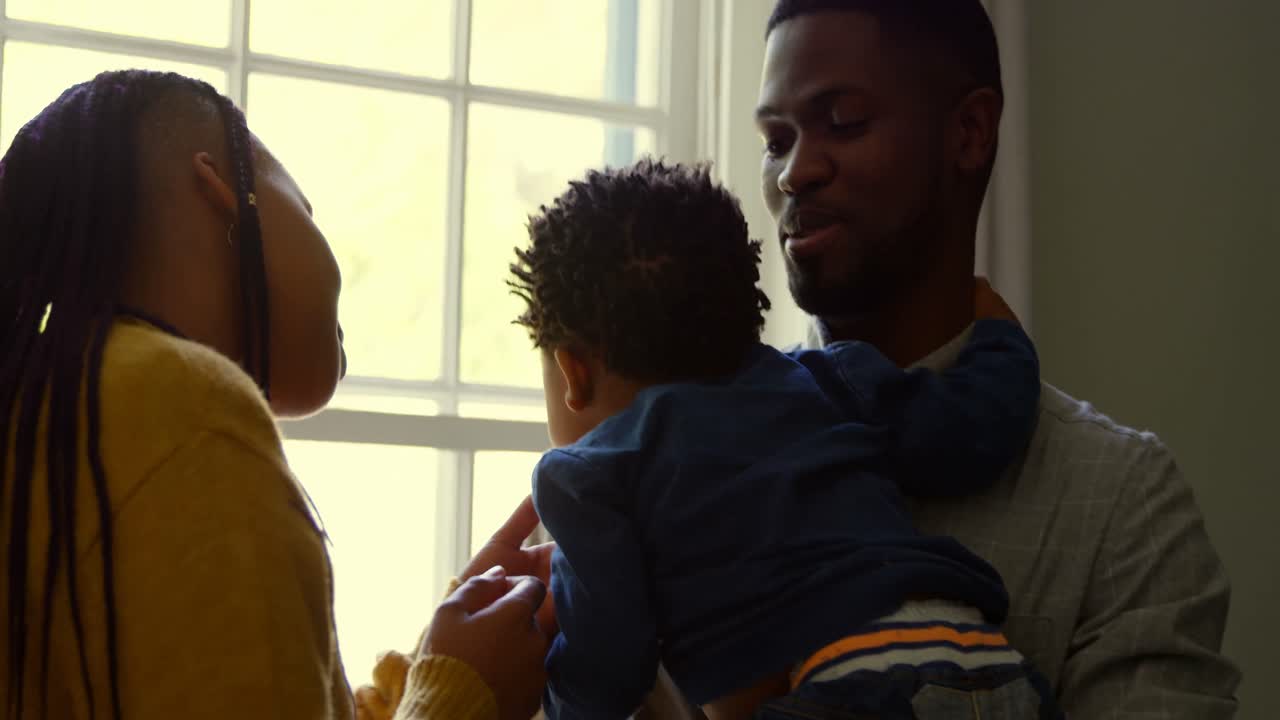 vista frontal de un joven padre negro sosteniendo a su bebé en un cómodo hogar 4k