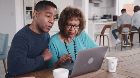 Hombre-Negro-De-Mediana-Edad-Ayudando-A-Su-Madre-A-Usar-Una-Computadora-Portátil-En-Casa,-De-Cerca