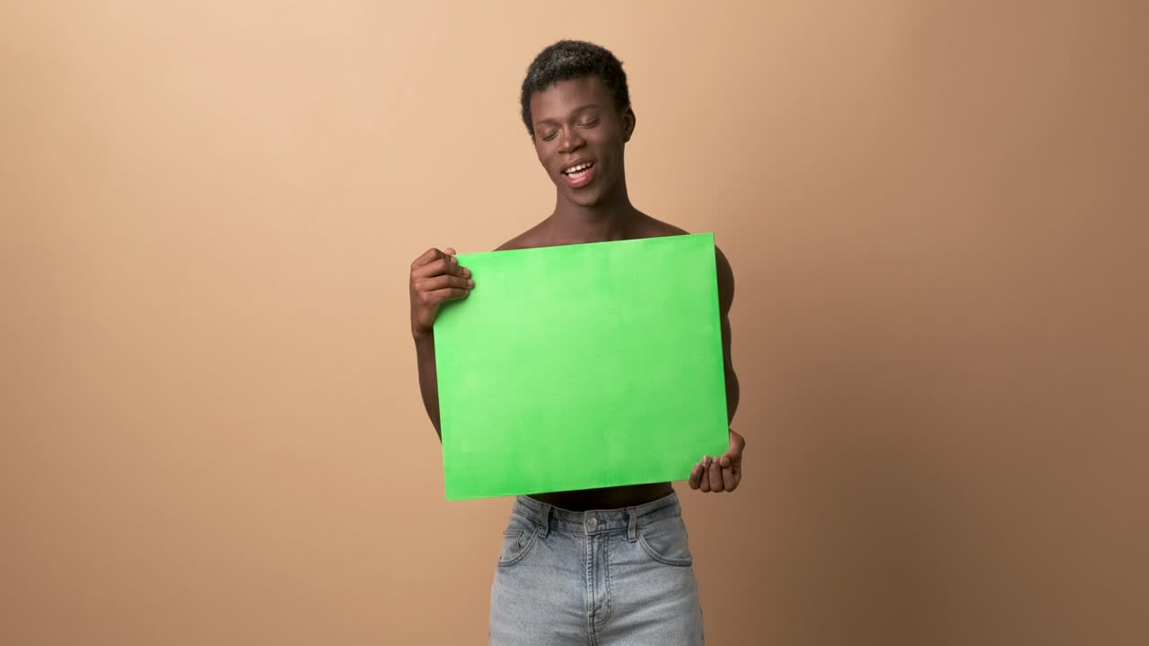 Happy young black shirtless man with a green chroma banner looking at camera with beige background